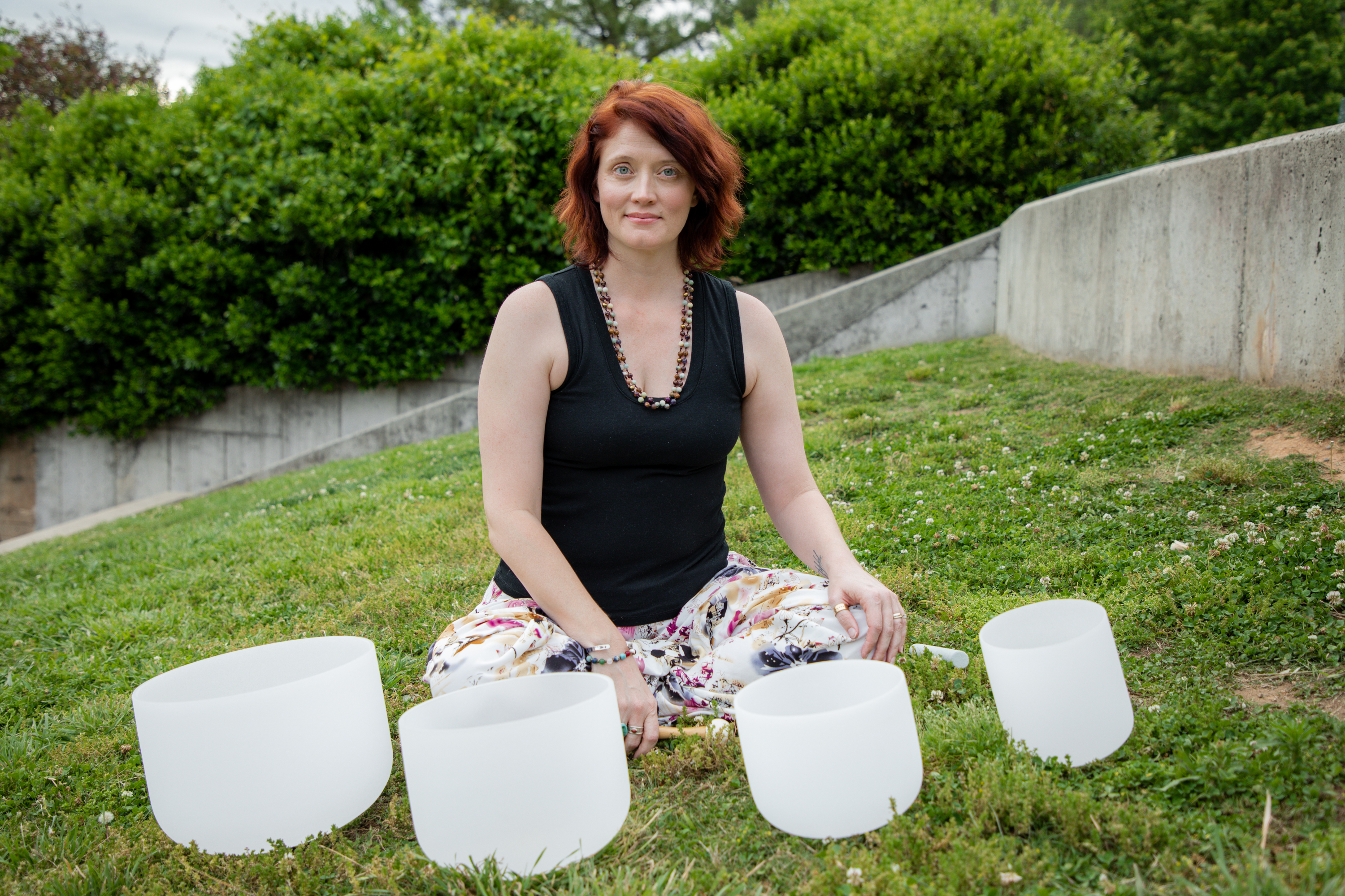 Carli Webb seated outdoors behind a row of crystal singing bowls