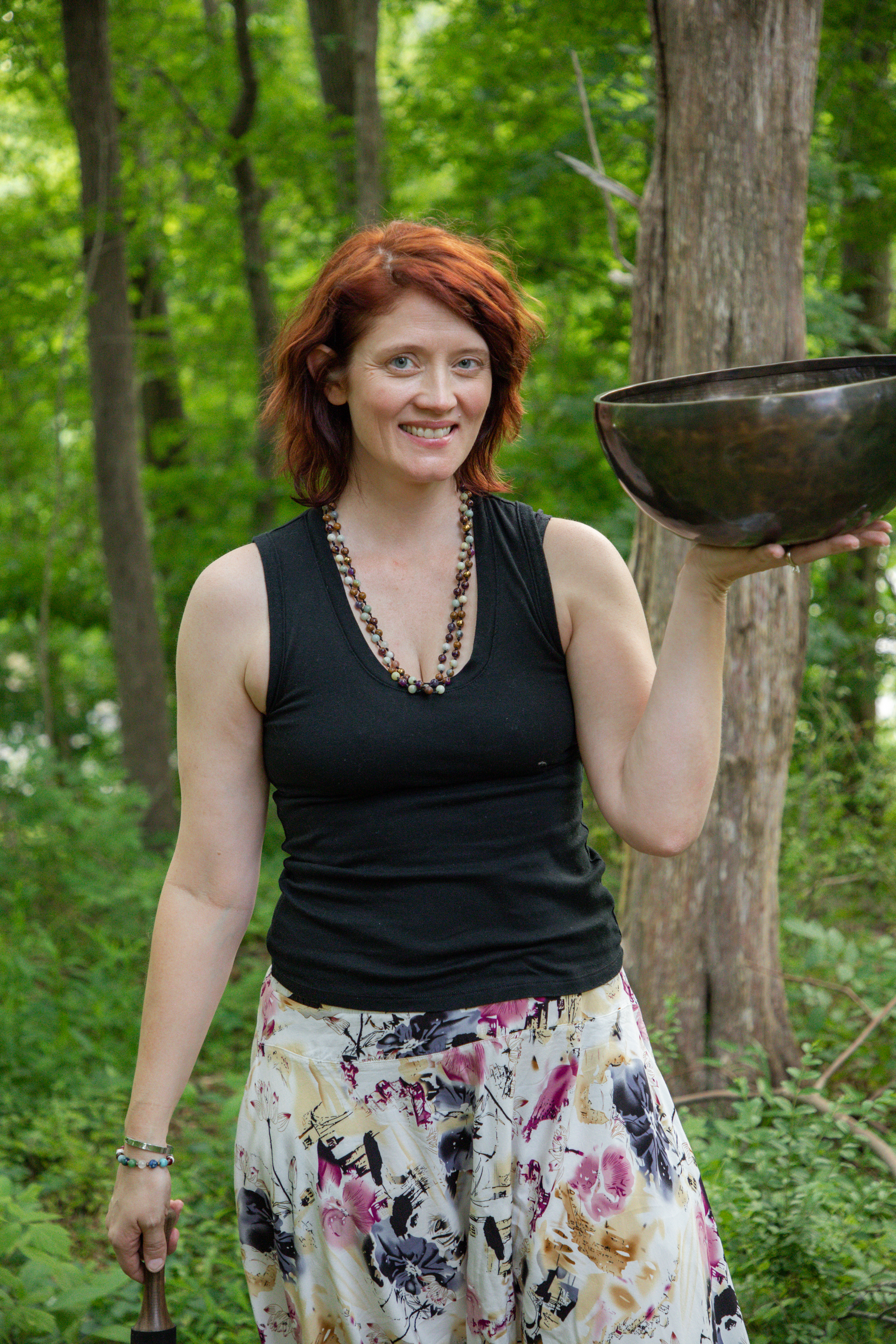 Carli Webb standing in the woods holding a bronze singing bowl